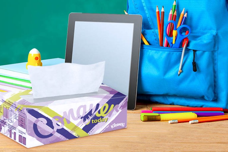 A Kleenex box, a tablet, a stack of books, and a backpack full of school supplies sit on a table.