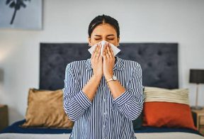 Woman blows her nose into a tissue in her bedroom